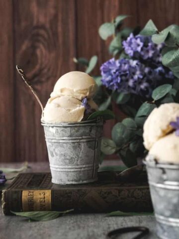 image of two steel buckets of basil ice cream with a rustic background and purple lilacs surrounding