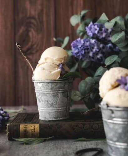 image of two steel buckets of basil ice cream with a rustic background and purple lilacs surrounding
