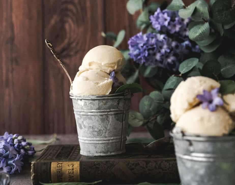 image of two steel buckets of basil ice cream with a rustic background and purple lilacs surrounding