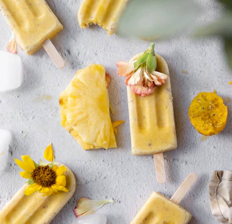 overhead shot of 4 prickly pear popsicles with pineapple and prickly pears on a bright white surface