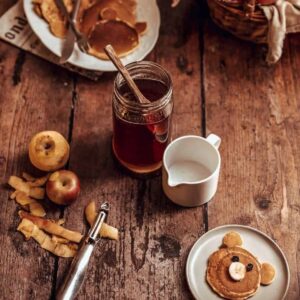 photo of a jar of apple peel syrup on a brown rustic background with a bear shaped pancake in the corner