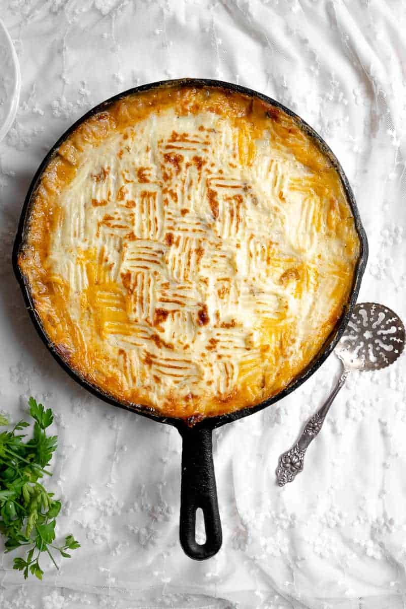 overhead shot of freshly baked cottage pie in a skillet on a delicate white tablecloth with a vintage serving spoon