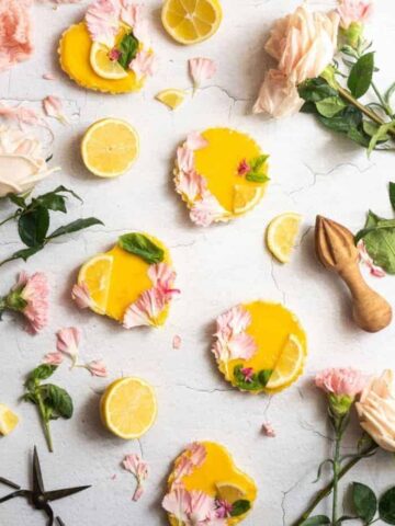 cover image of mini lemon basil tarts with 5 mini tarts on a concrete surface surrounded by rose and basil