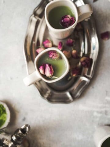 overhead shot of two mugs with beautiful green matcha and small rose bud