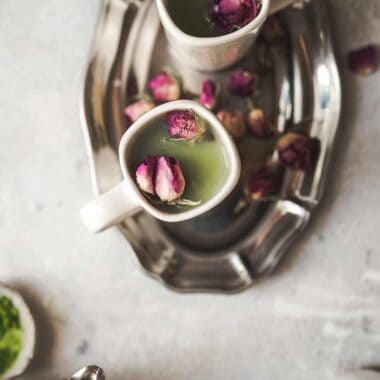 overhead shot of two mugs with beautiful green matcha and small rose bud