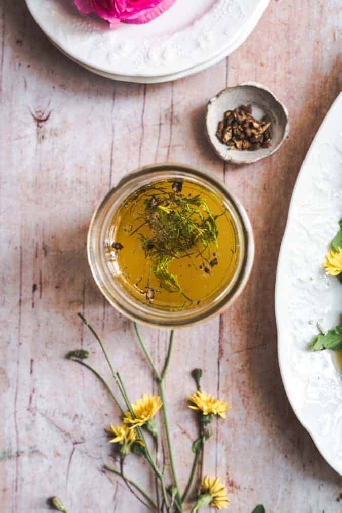 overhead shot of a jar of freshly made dandelion dressing topped with herbs on a wooden rustic background