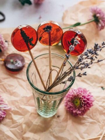 cup of honey lavender lollipops with lavender buds on a piece of brown parchment paper with flowers
