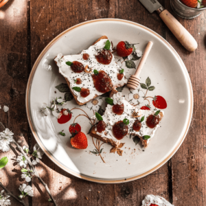 overhead shot of toast covered with mascarpone cheese with dollops of jam shaped like strawberries and mint leaves on a vintage plate with wild strawberries