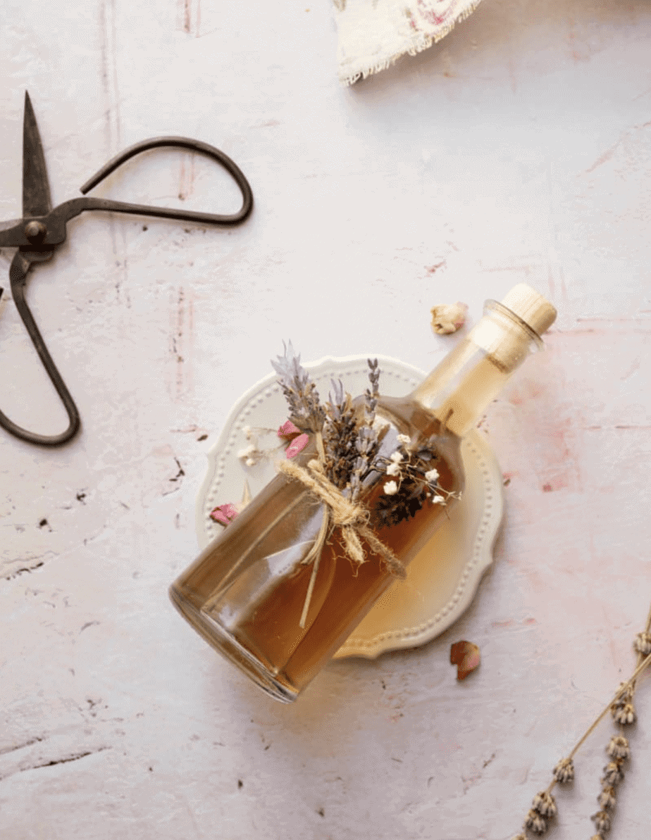 bottle of lavender honey simple syrup laying down on a pink surface with lavender tied to it as a gift