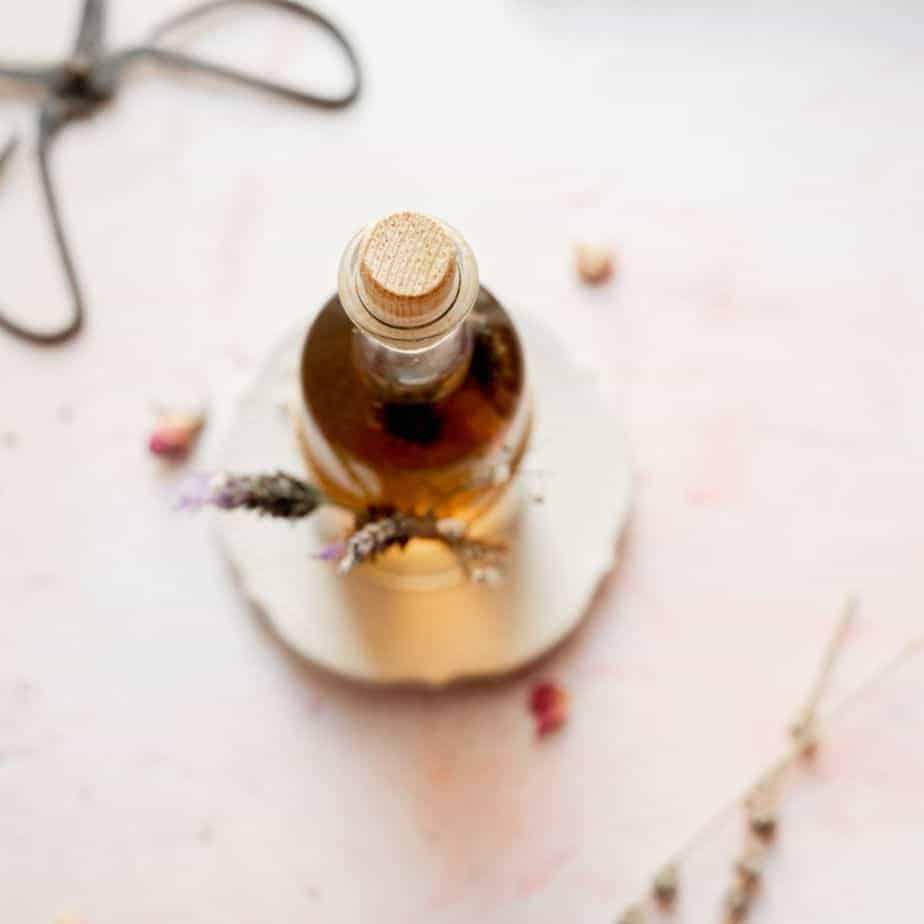 overhead image of lavender honey simple syrup, cork bottle with fresh lavender flowers on a pink backdrop