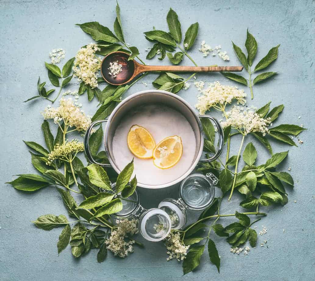 overhead shot of pot filled with sugar and lemon surrounded by leaves for elderflower syrup preparation