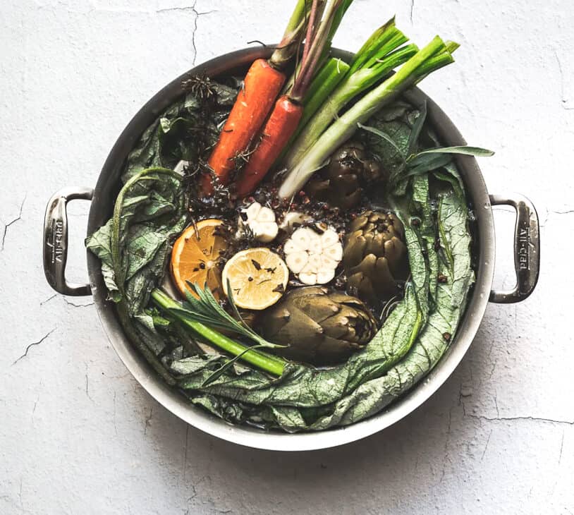 overhead image of big pot of stock with lemons carrots celery artichoke