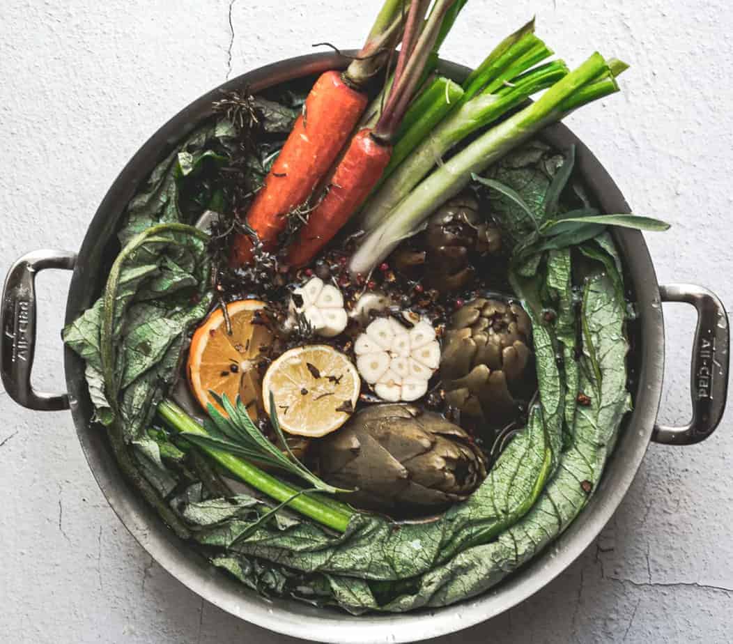 overhead image of veggies and herbs in a big pot of broth