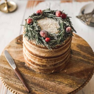 close up shot of cake with candied rosemary wreath on top on wooden cake stand