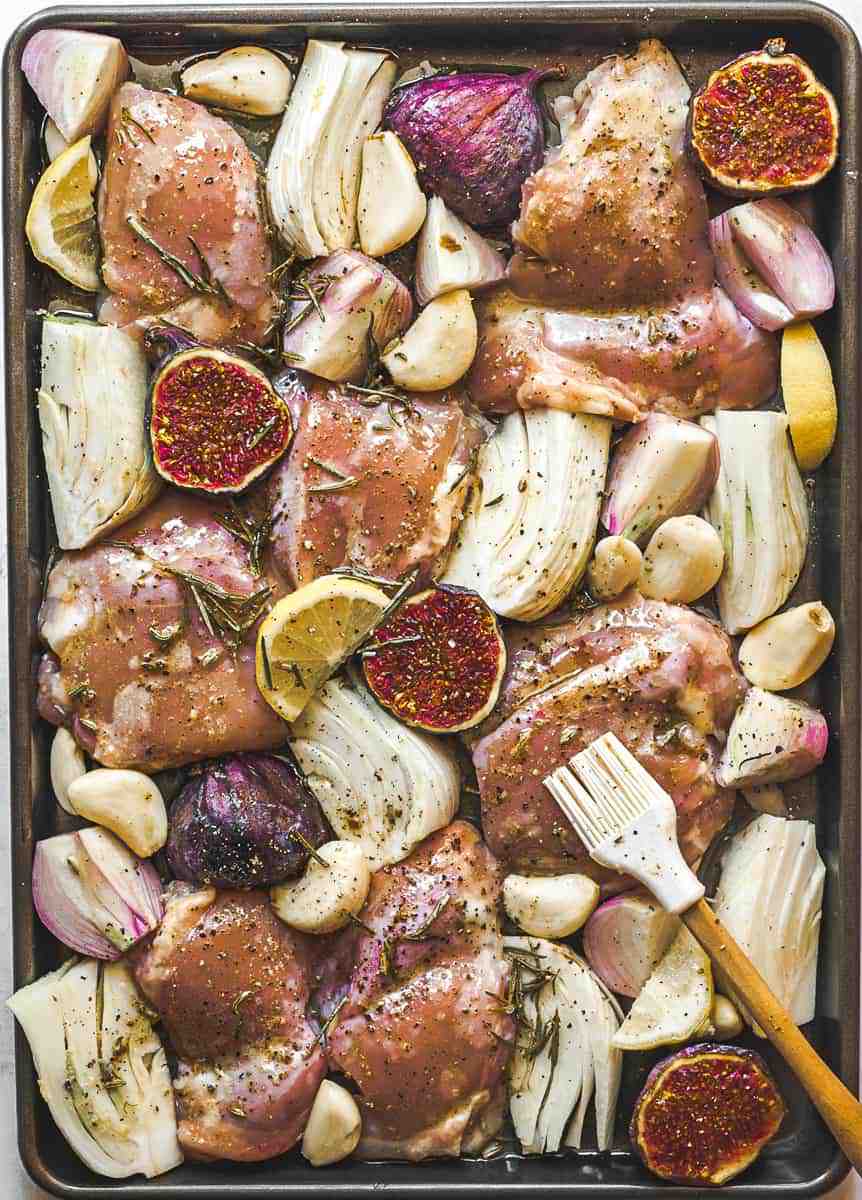 prep shot of uncooked chicken thighs arranged with ingredients in oven roasted chicken thighs with fig and fennel, brushed with brown butter