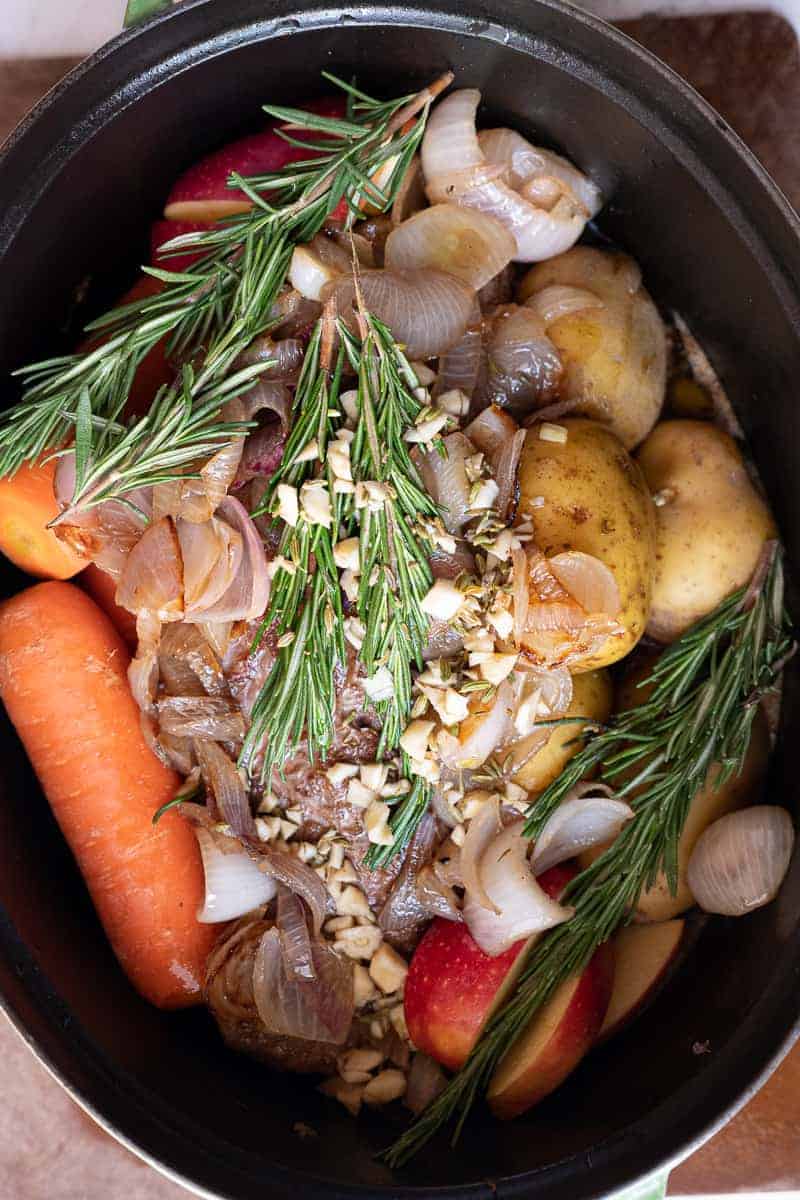 overhead close up shot of brisket with herbs and marinade in dutch oven