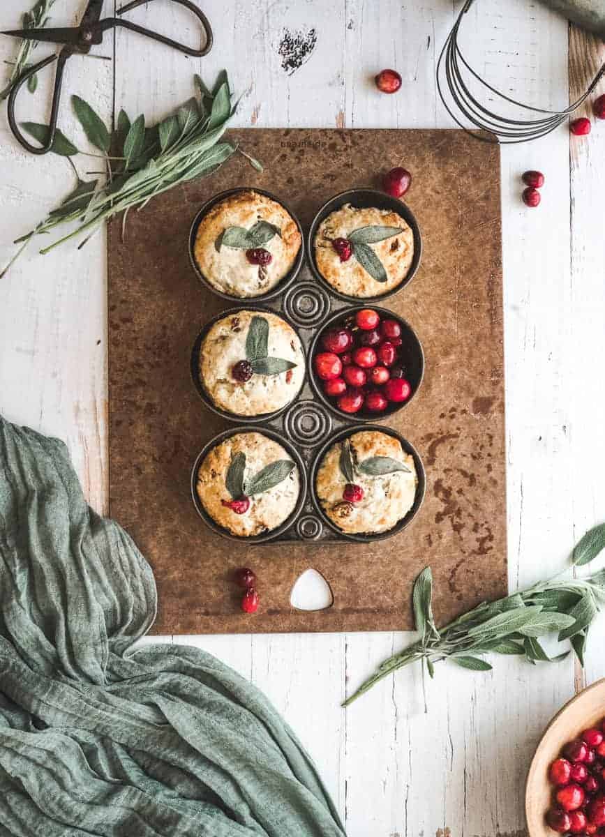 image of cranberry sage buttermilk biscuits - overhead shot of biscuits in a vintage in with sage leaves and fresh cranberry garnish