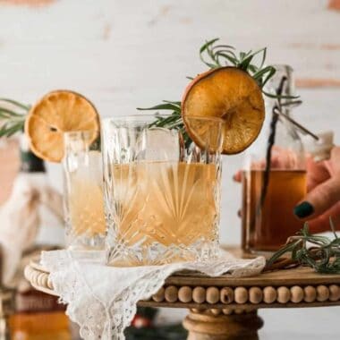 close up whisky crystal glass with yellow tinted cocktail with a dried orange garnish with rosemary