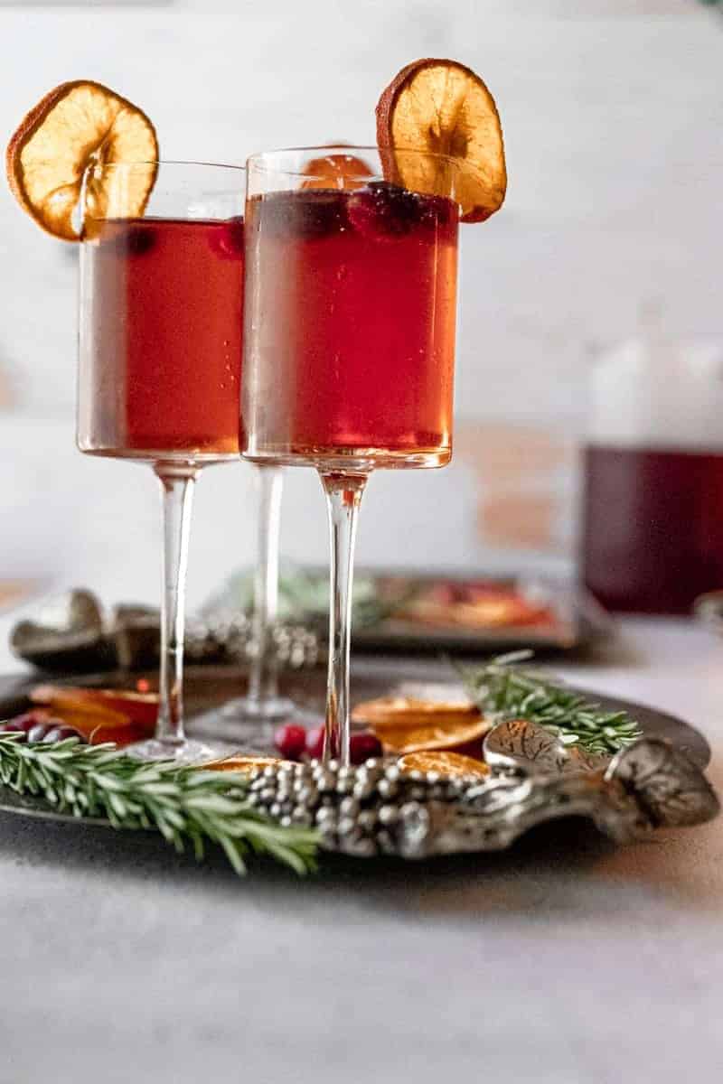 tall glasses filled with cranberry juice and champagne on a silver tray with rosemary and dried orange slices