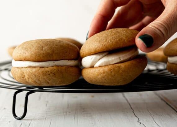 woman's hands with dark green finger nails placing the top half of a whoopie pie on frosted cookie