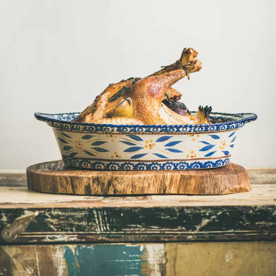 ceramic dish with whole roasted chicken with legs tied with lemon stuffed with herbs and garlic
