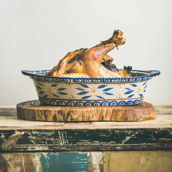 Roasted whole chicken for Christmas eve celebration table on rustic wooden board, light grey wall background, copy space, square crop