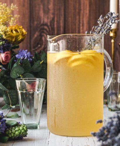 close up pitcher of lemonade with a rustic background and rustic wooden table top, background has basket of fresh flowers