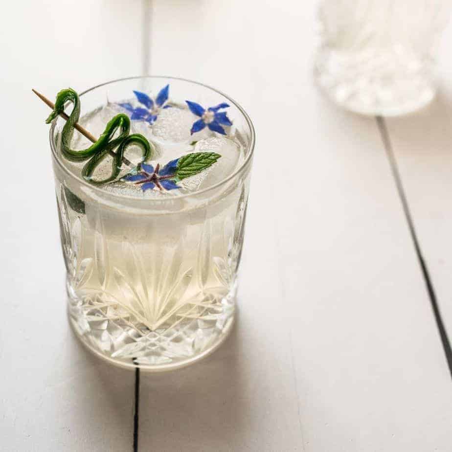 close up glass cucumber borage gin and tonic - whisky glass with cucumber garnish and two dainty borage flowers floating on top