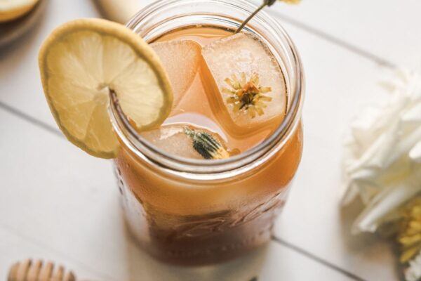 overhead image dandelion root iced tea, mason jar filled with iced tea with an ice cube with dandelion flower in it
