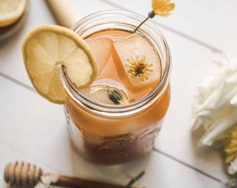 overhead image dandelion root iced tea, mason jar filled with iced tea with an ice cube with dandelion flower in it