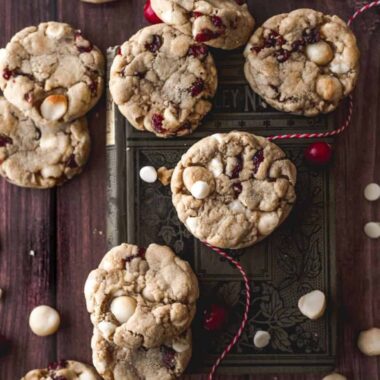 close up overhead image of chewy white chocolate macadamia cranberry cookies on a green book on top of a dark brown surface for a rustic look