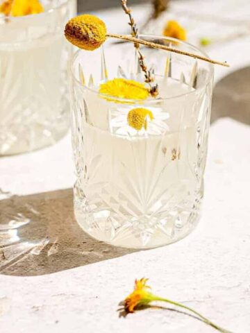 cropped close up shot of dandelion lemonade with dandelion and chamomile flower floating on top