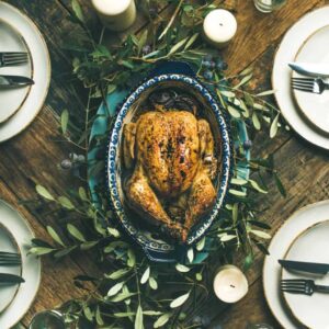 overhead shot of rustic wooden table with roasted chicken surrounded by table setting