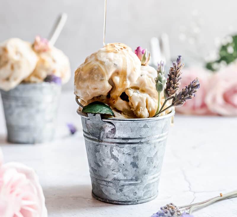 image of small bucket filled with lavender ice cream with honey being poured on it and fresh lavender flowers