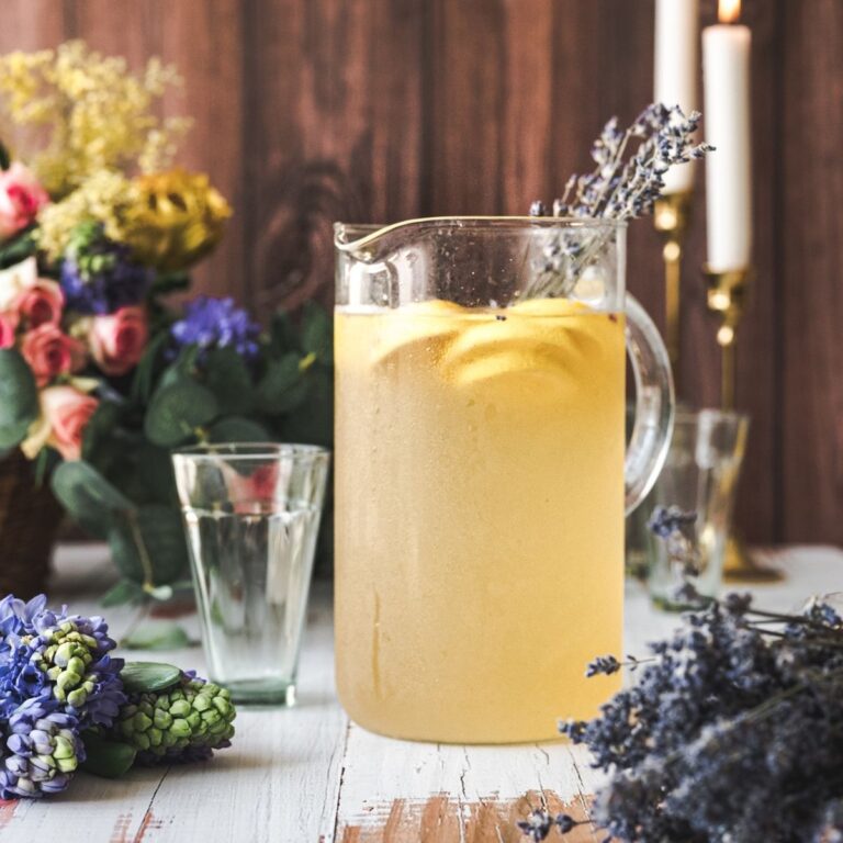 close up pitcher of lemonade with a rustic background and rustic wooden table top, background has basket of fresh flowers