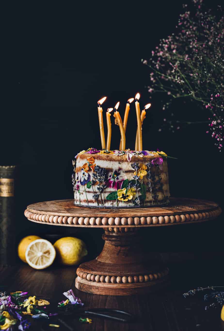 wooden cake stand with small 6" naked cake, decorated with edible flowers, with beeswax candles on top lit