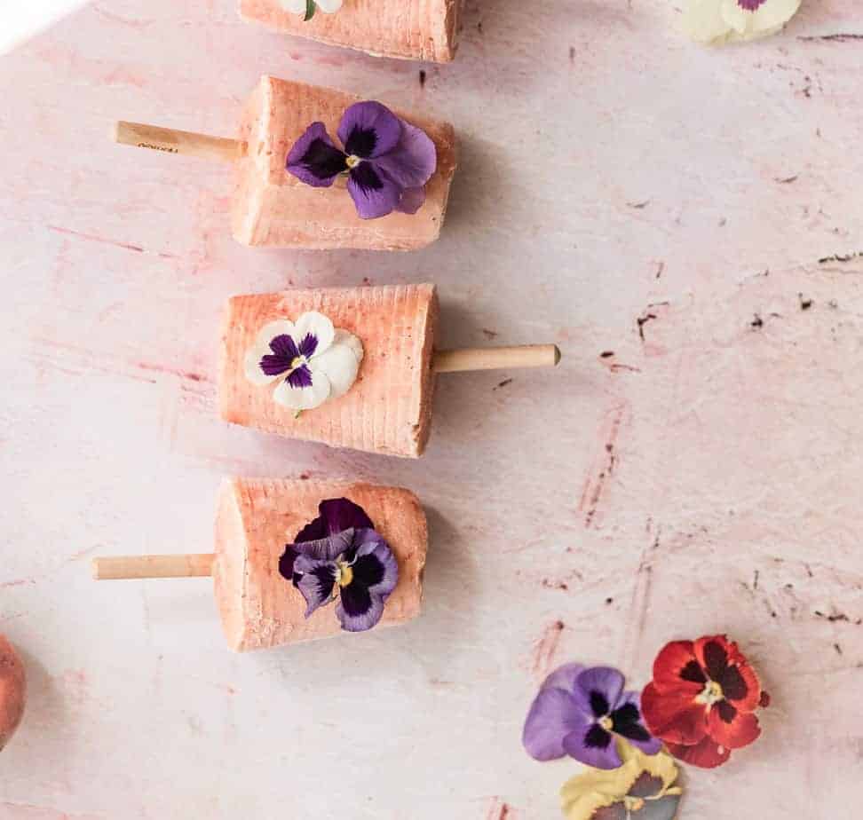 overhead shot of peaches and cream popsicles with edible pansies on top in a line