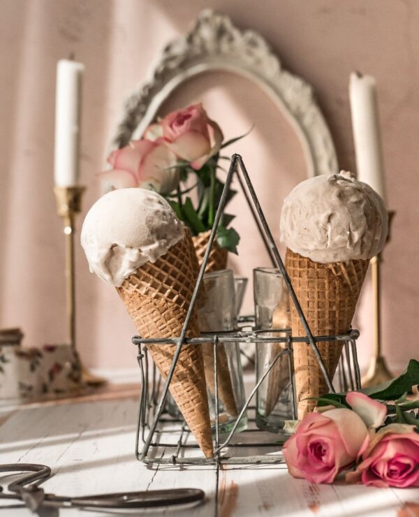 image of vintage glass carrier filled with sugar cones, and pink ice cream scoops, garnished with pink roses, and in front of vintage white frame and two candlle sticks