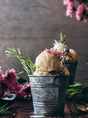 up close image of scoops of rosemary ice cream with sprigs of green rosemary sticking out in bowls in vintage buckets