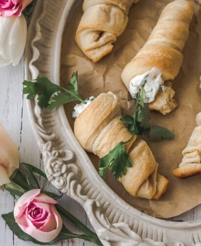 vintage dish surrounded by flowers with carrot shaped stuffed crescent rolls with cream cheese and parsley coming out of the top to look like carrots