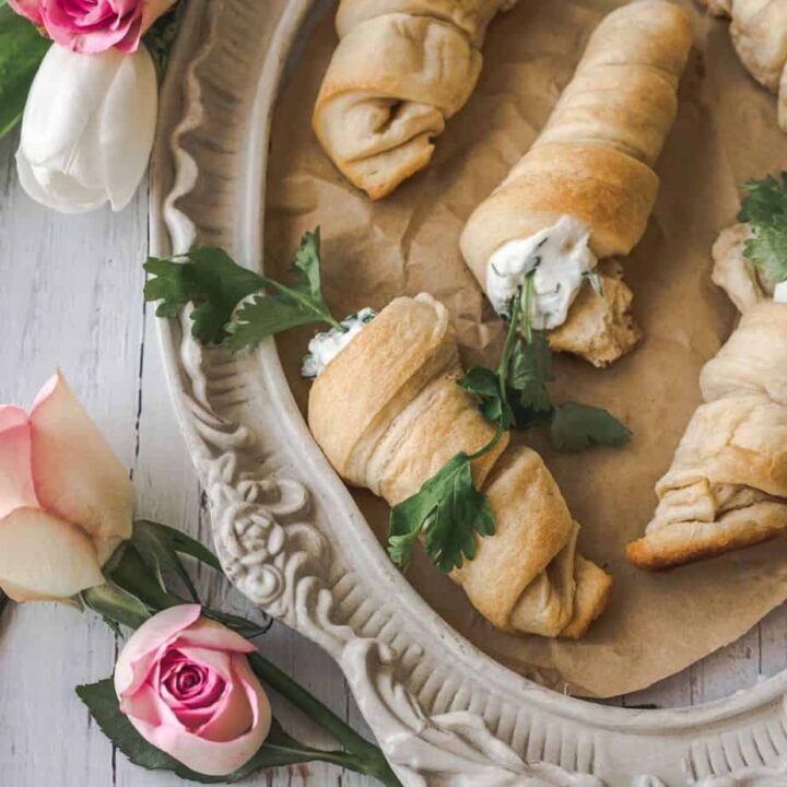 vintage dish surrounded by flowers with carrot shaped stuffed crescent rolls with cream cheese and parsley coming out of the top to look like carrots