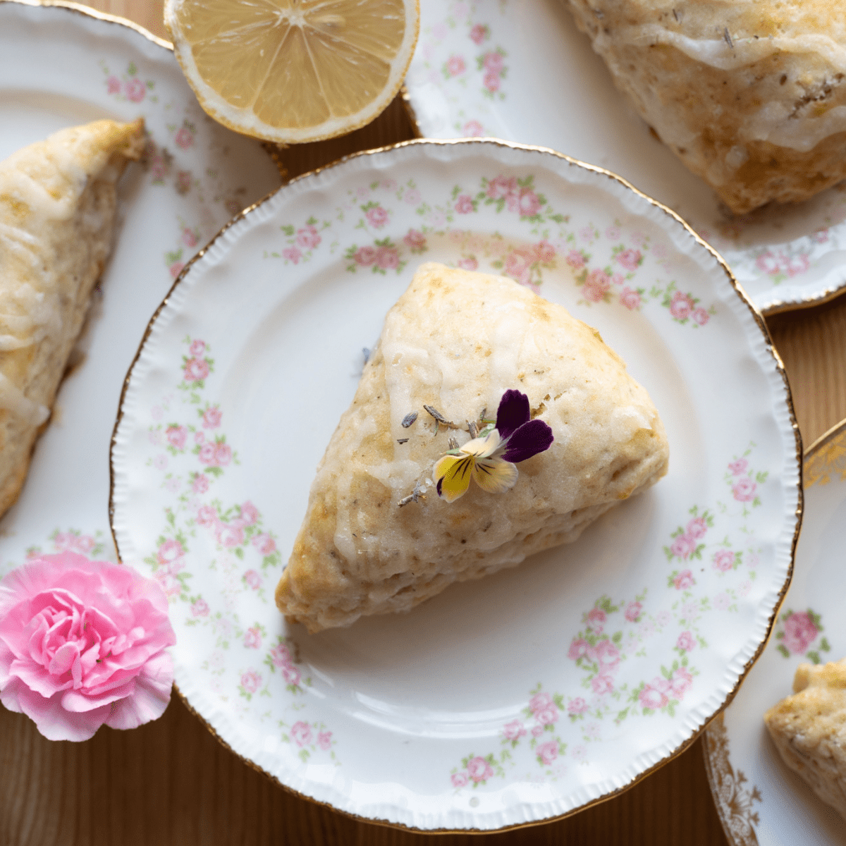 overhead image of scone with little pansy on top on a tea plate with roses
