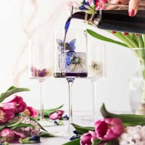 cover image of butterfly pea syrup three glasses with flower icecubes with woman's hand with pink nails pouring bright blue butterfly pea syrup into glass