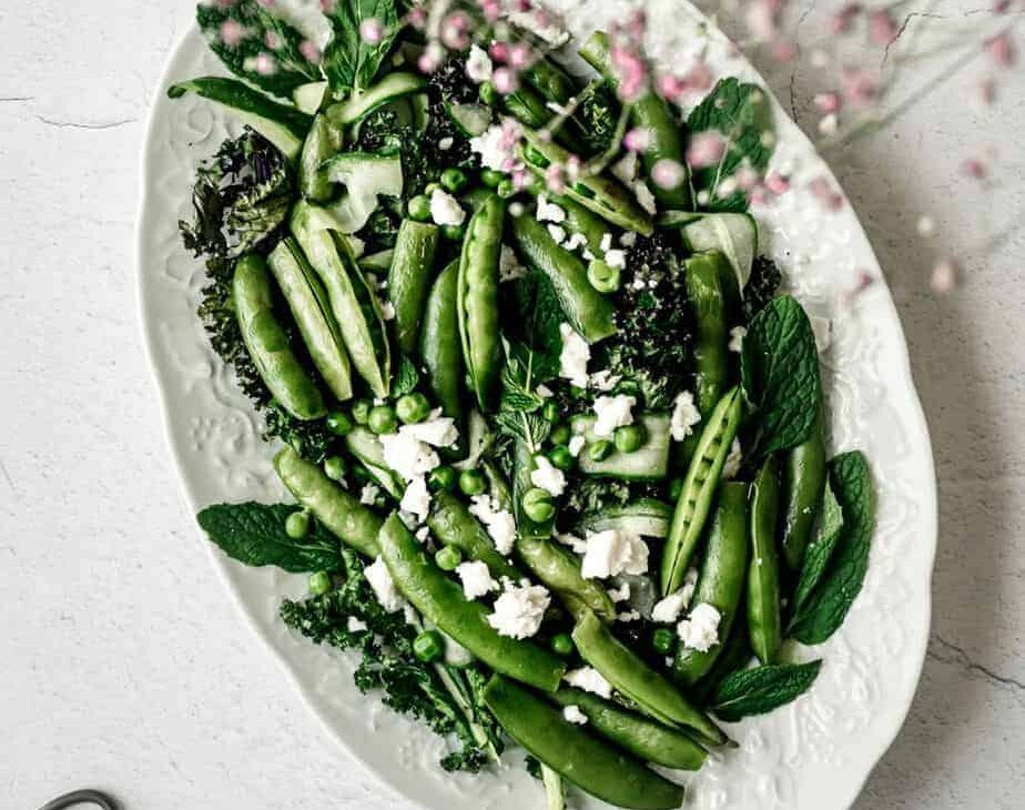 overhead image of peas and greens in a dish with feta cheese with purple flowers