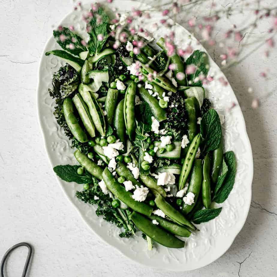 overhead image of peas and greens in a dish with feta cheese with purple flowers