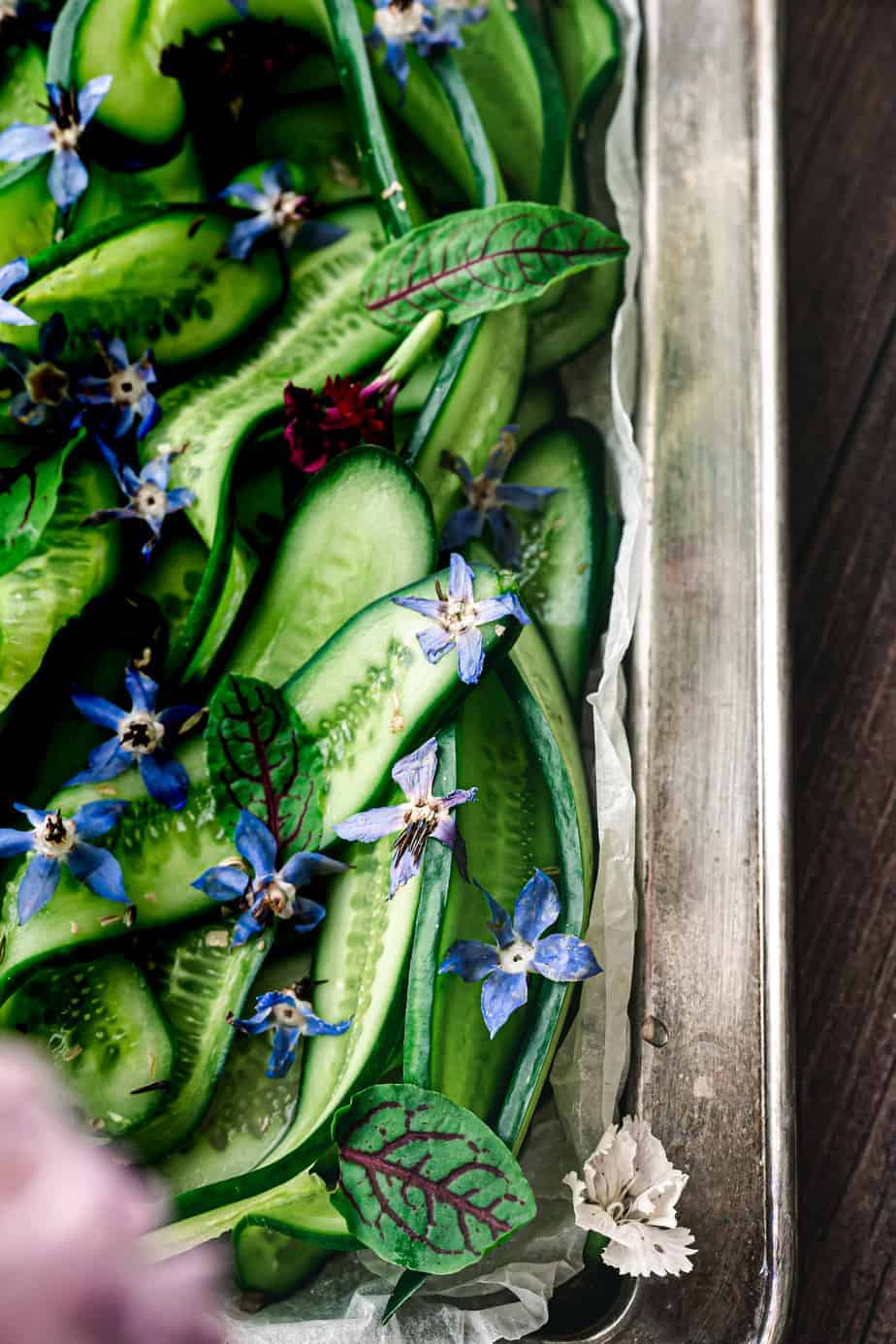 close up shot of thinly sliced cucumber and borage flowers