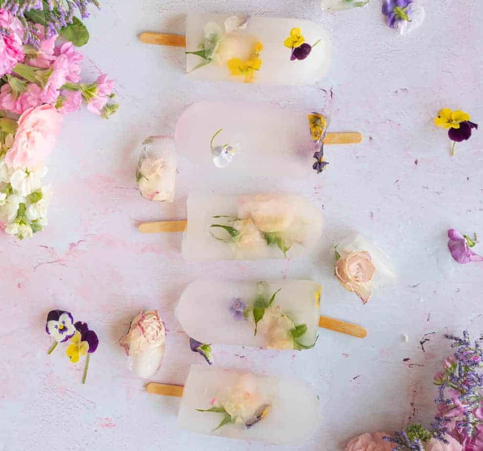 overhead shot of light pink surface with clear popsicles filled with edible flowers