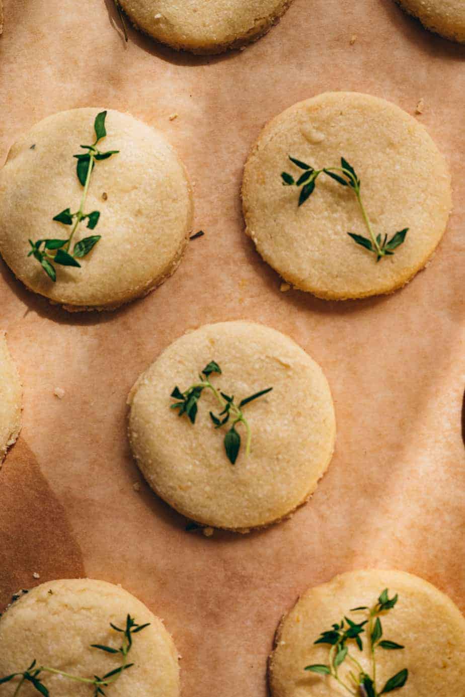 Brown parchment paper with three buttery thin round shortbread cookies with fresh thyme garnish on top