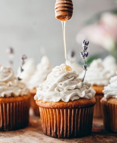 close up image of a perfect cupcake with lavender honey buttercream piped on top with a honey comb stick dripping honey onto cupcake