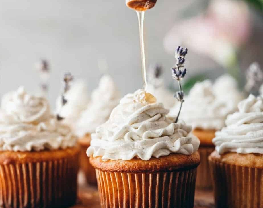 close up image of a perfect cupcake with lavender honey buttercream piped on top with a honey comb stick dripping honey onto cupcake